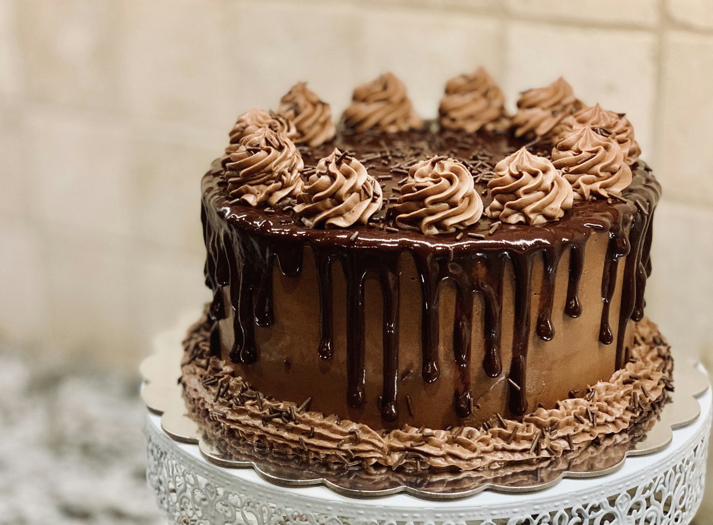 A towering chocolate drip layer cake, photographed close and warm