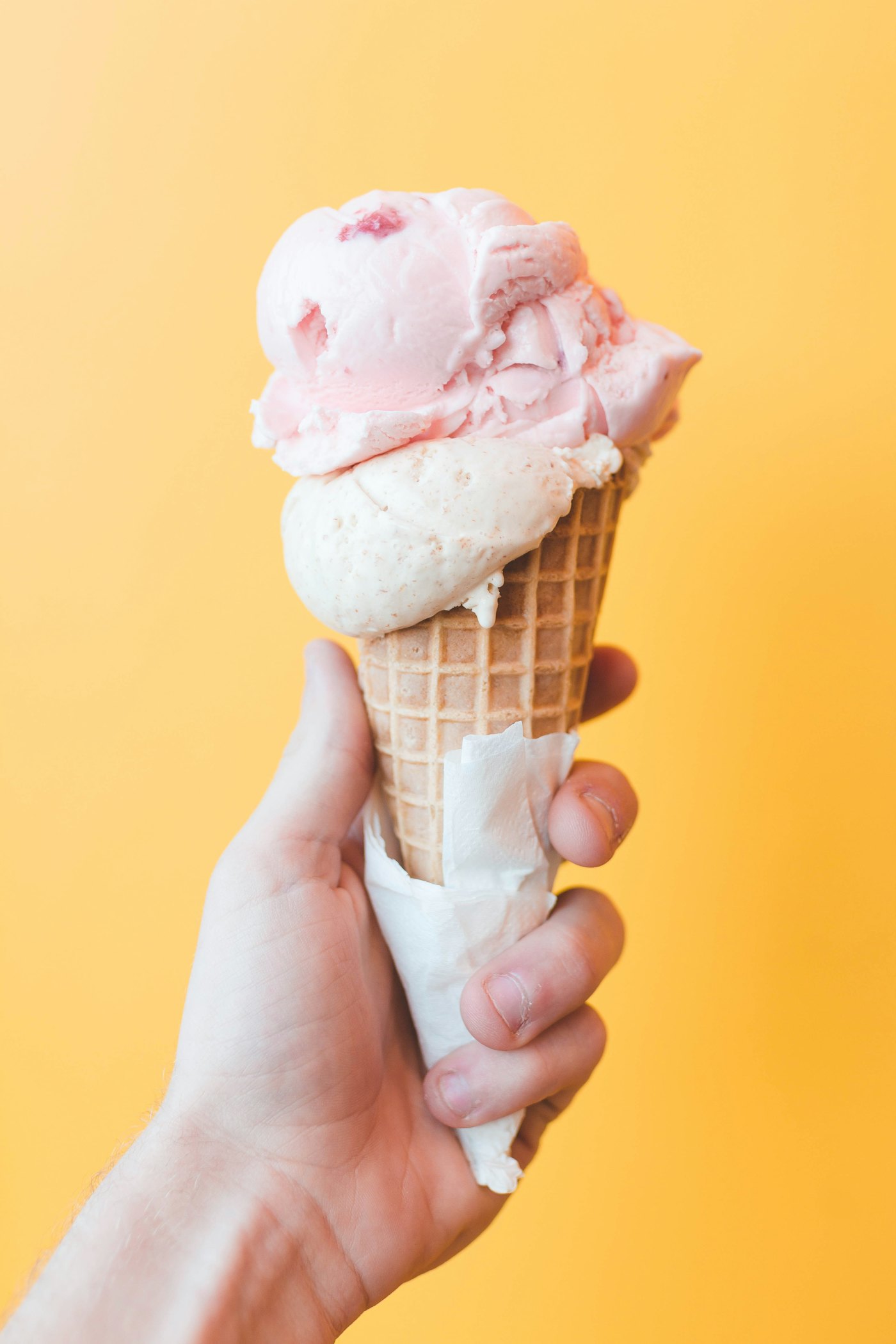 A soft-serve ice cream cone held in hand against a warm peach backdrop