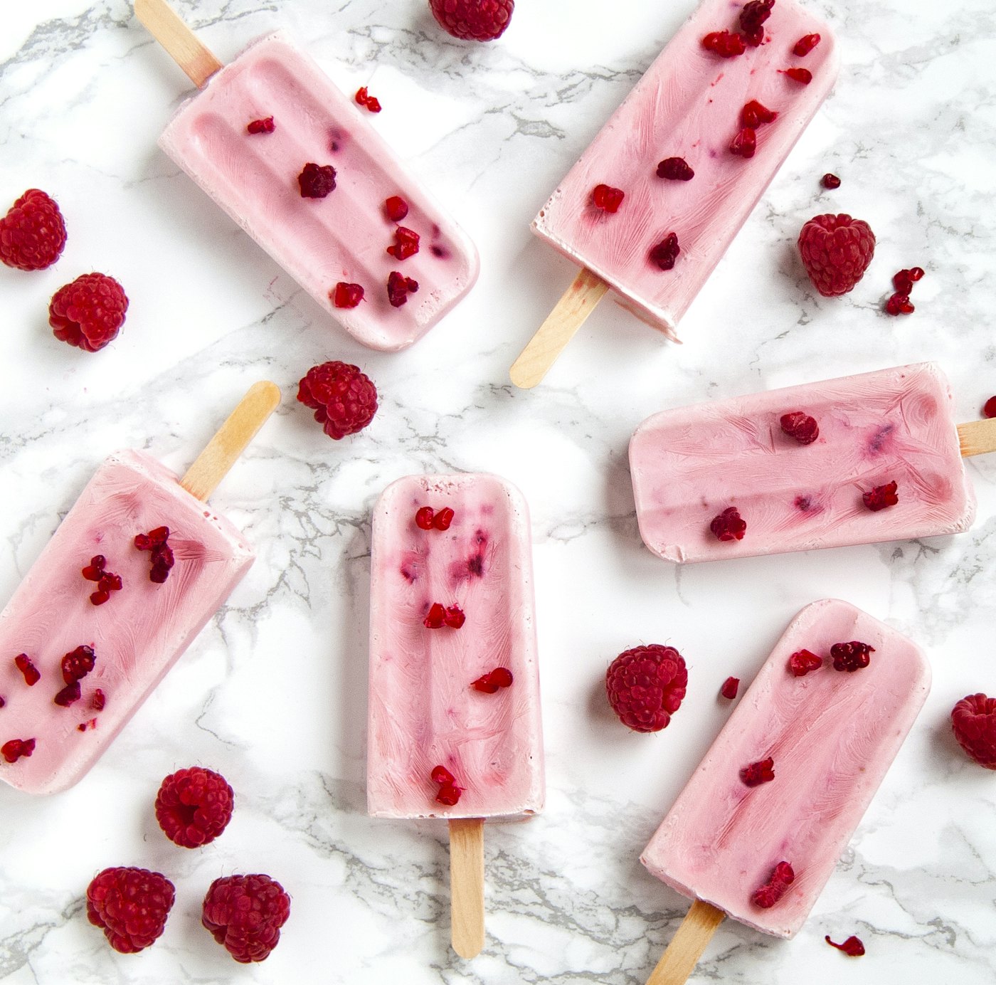 Blush-pink raspberry popsicles arranged on white marble